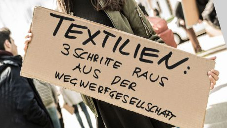 Schild auf einer Demonstration: Textilien - 3 Schritte raus aus der Wegwerfgesellschaft